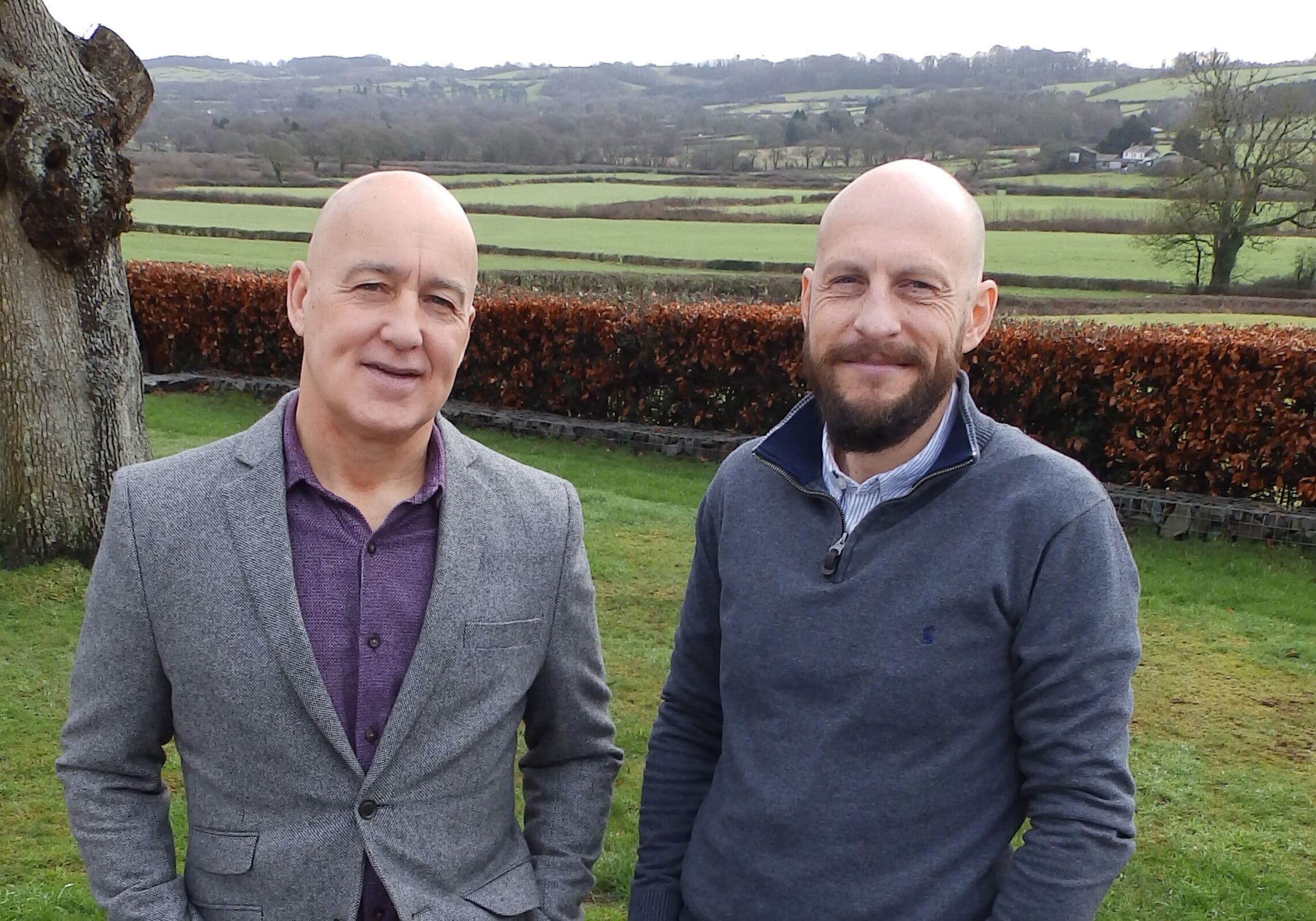 two businessmen standing next to one another outside a house with a green horizon on the background